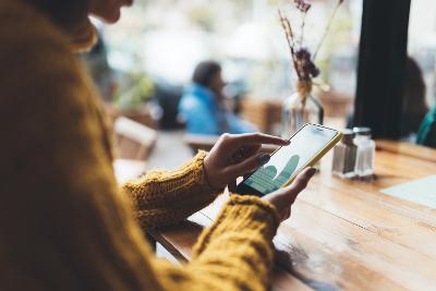 Close up of woman in a yellow jumper typing on a smartphone while sitting at a cafe table